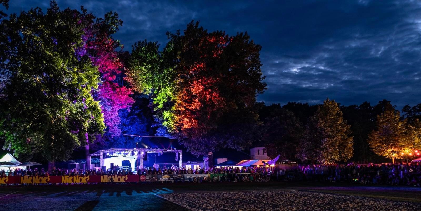 Farbig angestrahlte Bäume und Bühne in der Abenddämmerung