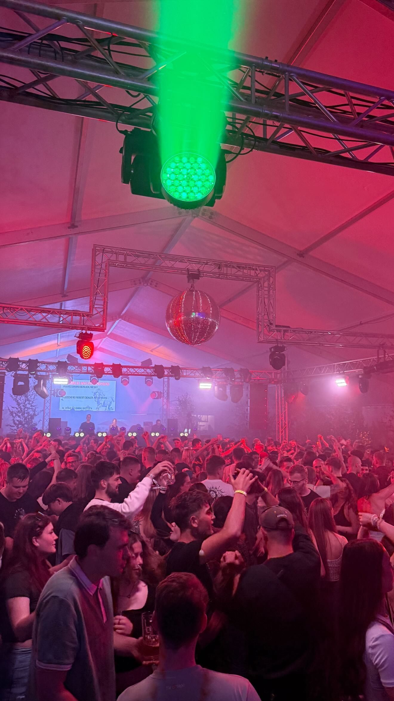 Grüner Lichtstrahl und Spiegelkugel über tanzendem Publikum in rotem Licht, Festzelt in Horka