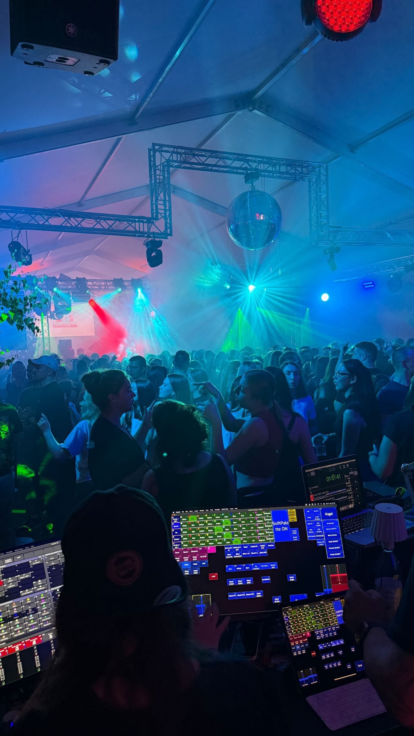 Festzelt in blauem Licht mit Lasern, im Vordergrund die Lichtsteuerung mit Touchscreens